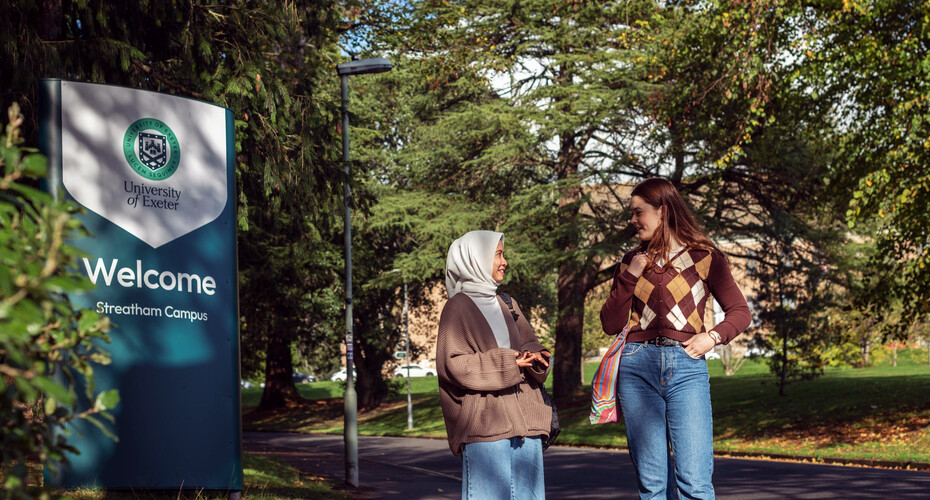 Two students talking and smiling beside a sign reading 'Welcome to Streatham Campus'