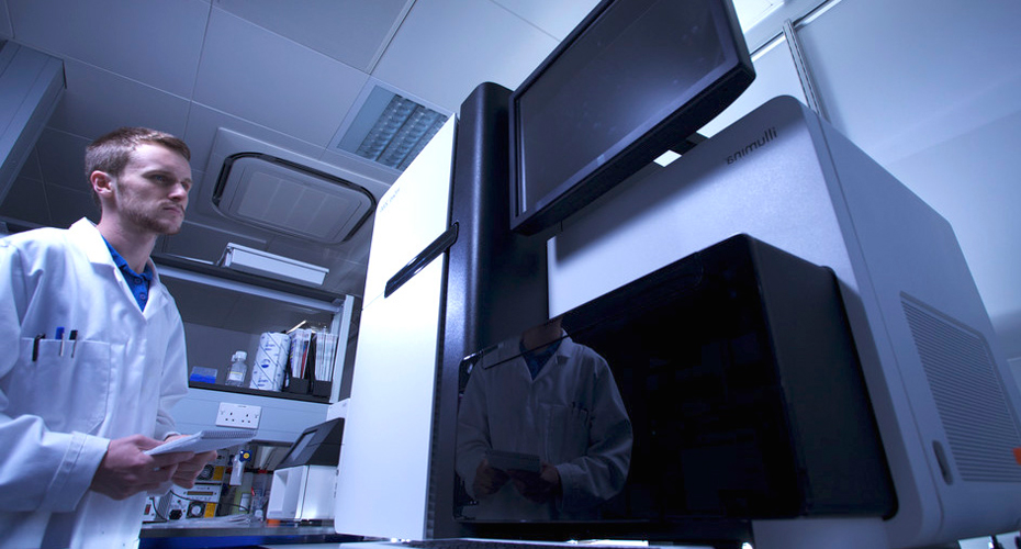 A researcher wearing a lab coat using a sequencing machine