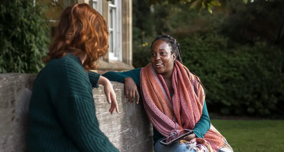 Two people chatting on a bench outside