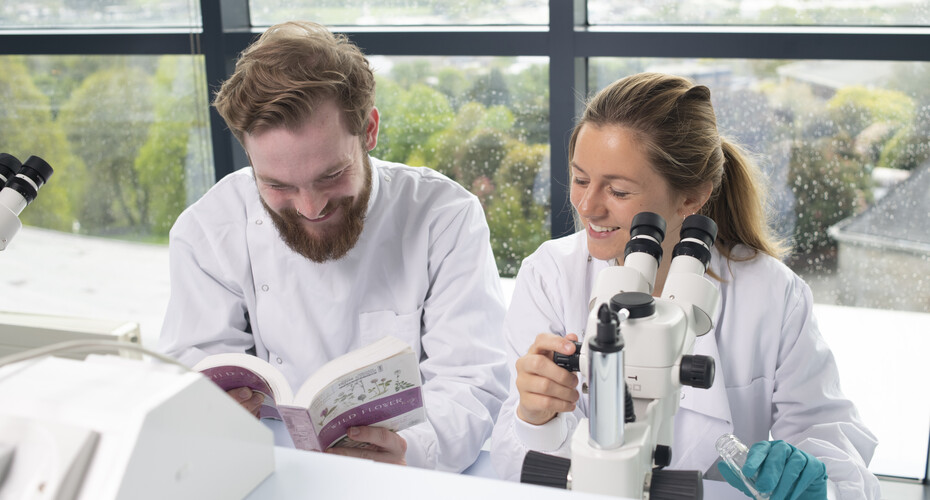 Two Biosciences students working together with a textbook and microscope